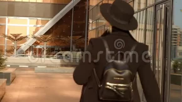 肖像年轻迷人的微笑女人戴着帽子和黑色外套走在市中心的街道上感到时尚快乐视频的预览图