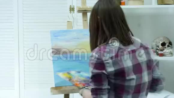 一个年轻的女人在画布上画一幅画站在画架后面在一个大气的车间里时间唇视频的预览图
