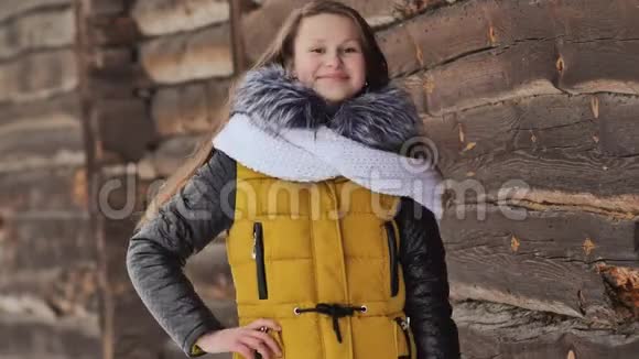 穿着冬装的年轻漂亮女孩正对着镜头在一座木屋的背景上摆姿势视频的预览图