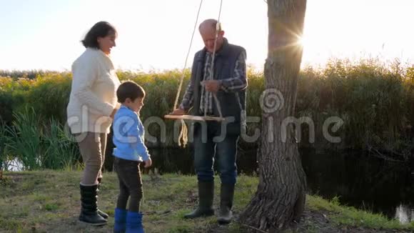 奶奶和爷爷在树上荡秋千孩子们在阳光下户外活动视频的预览图