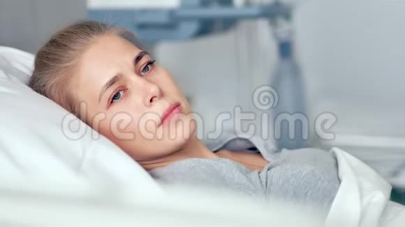 躺在医院房间里的年轻女性病人伤心难过的女人在现代诊所里思考生活视频的预览图