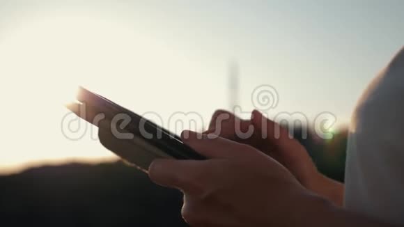 在日落时分一个女孩用平板电脑在太阳下的大海背景下工作视频的预览图