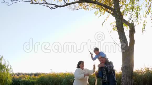 快乐的孩子和祖父母把绳子扔在树上在阳光明媚的天气里荡秋千视频的预览图