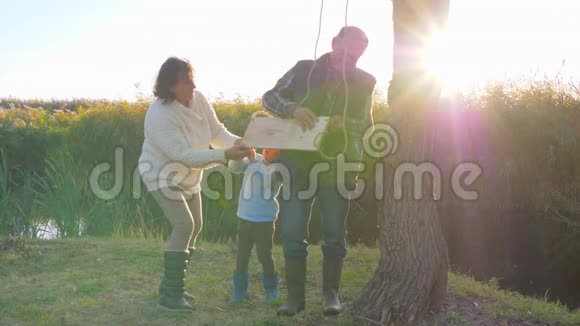 爷爷和奶奶在树上荡秋千在湖边的空地上为好孩子荡秋千视频的预览图