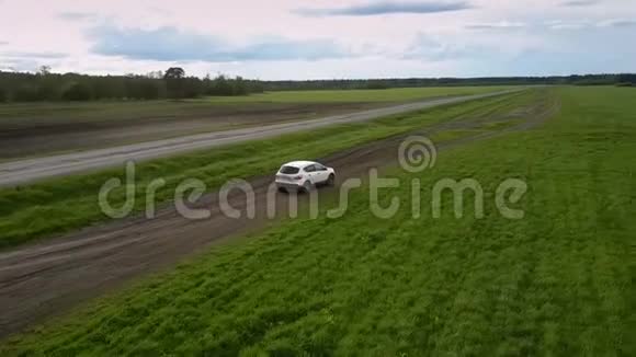 白色车辆沿着绿色田野的棕色地面道路行驶视频的预览图