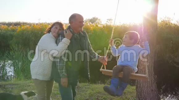 微笑的女人拥抱丈夫和孙子在大自然中摇摆视频的预览图