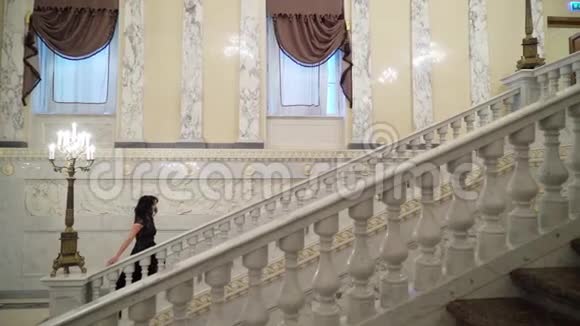 年轻的黑发女子穿着黑色晚礼服在或酒店的大理石石梯上楼视频的预览图
