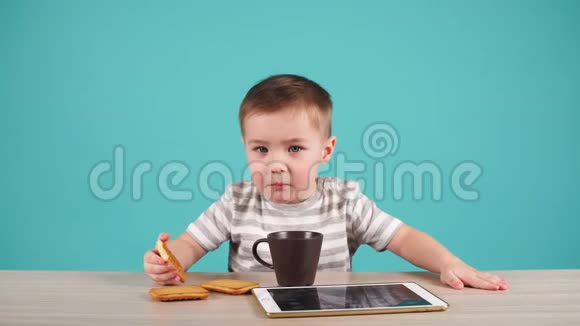 桌子旁的小男孩吃一块饼干被隔离在蓝色上视频的预览图
