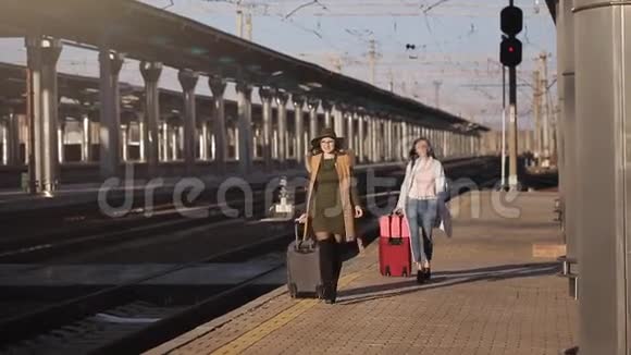 火车站的两个女孩带着手提箱在站台上等火车视频的预览图
