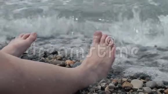 一个孩子的腿特写被波浪淹没了卵石沙滩喧闹的海浪拍打着孩子们双腿视频的预览图