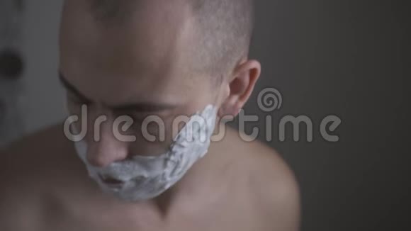 用剃刀刮脸的人的特写借助特殊的泡沫镜子前的房子视频的预览图