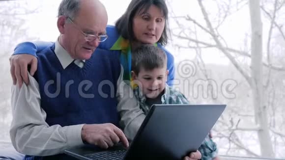 幸福的家庭祖父母和孙子孙女在大窗户附近玩电脑视频的预览图