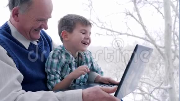 一个带着笔记本电脑的祖父坐在家里的笑男孩视频的预览图