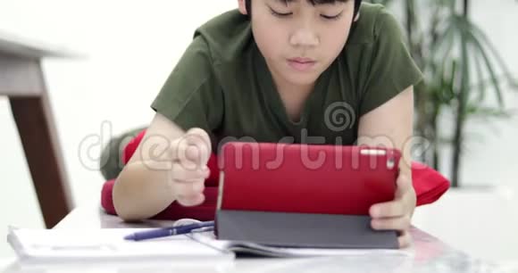 亚洲男孩在家里用平板电脑和耳机做作业视频的预览图