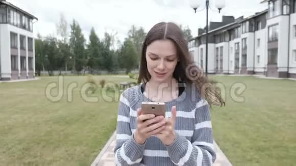 美丽的黑发女人正在手机上读到一些东西走在家附近视频的预览图