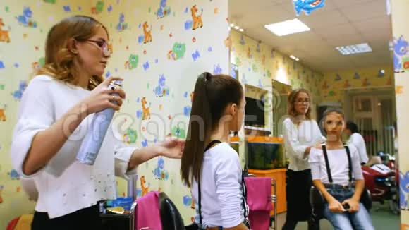 理发师和小女孩美发沙龙里的有趣孩子用发胶固定马尾辫儿童理发店视频的预览图