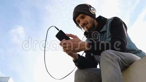 低射青年坐在背光和听音乐天空背景视频的预览图