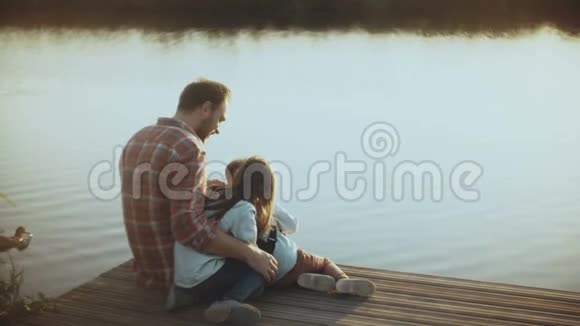 有两个孩子的白人看水鸟快乐的爸爸和孩子们坐在日落湖码头上童年4K视频的预览图