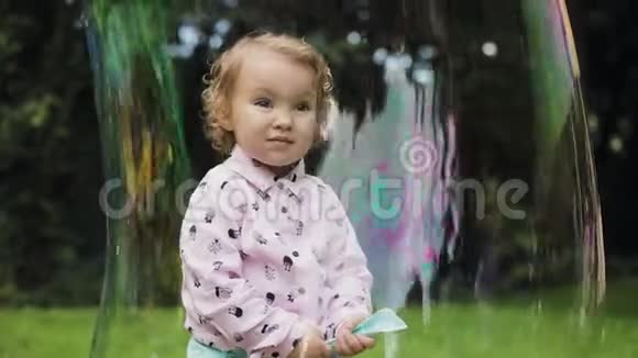 小卷曲的女孩在巨大的泡沫中感到快乐慢动作泡泡秀视频的预览图