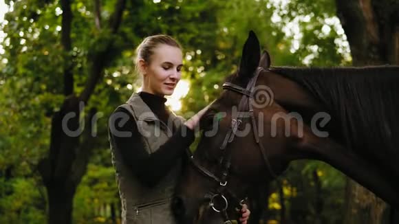 在阳光明媚的日子里微笑的女人正棕色的马头站在森林里视频的预览图