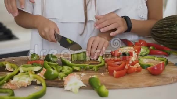 妈妈在家厨房教女儿切蔬菜女孩们切红和青椒做沙拉视频的预览图