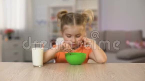 快乐的小女孩吃玉米片和牛奶坐在家里的桌子上健康的食物视频的预览图