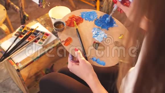 女艺术家拿着调色板与蓝色和红色的油彩和绘画图片特写视频的预览图