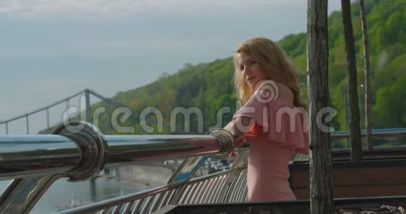 站在阳台上欣赏美丽的河流和美景的迷人金发女孩的肖像视频的预览图