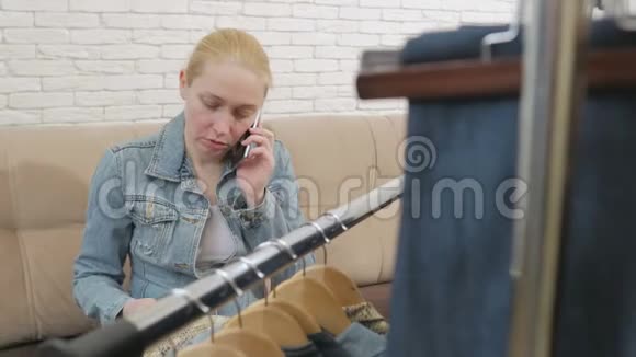 坐在沙发上的女人打电话检查挂在衣架上的一套牛仔裤视频的预览图
