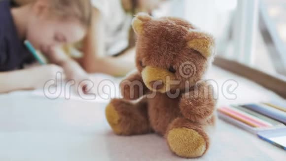 泰迪熊在特写镜头中两个女孩在模糊的背景下画画视频的预览图