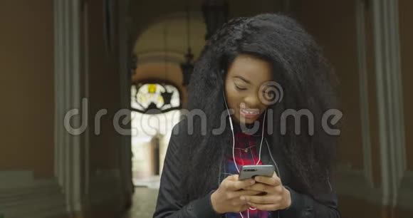 可爱的年轻非洲女孩带着美丽的微笑在通过手机发短信和上网时表达了她的惊讶之情视频的预览图