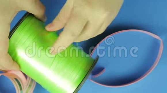 女性用剪刀从线圈中剪出绿色胶带蓝色背景视频的预览图
