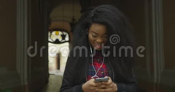 情感肖像美丽快乐的非洲女孩微笑和短信通过手机户外4K录像视频的预览图