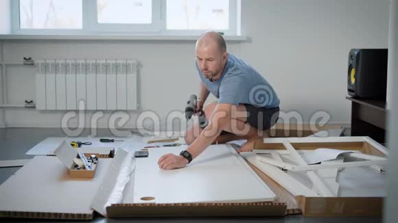 穿着蓝色T恤和黑色短裤的休闲男子为他的公寓组装新桌子视频的预览图