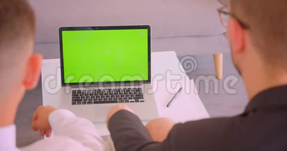 两位成功商人在办公室室内使用带有绿色屏幕的笔记本电脑的特写后景肖像视频的预览图