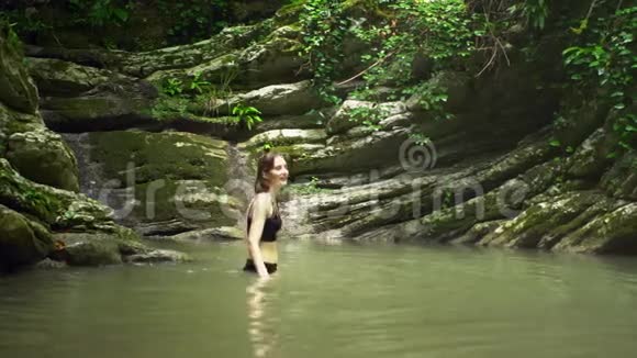 在热带森林的小山湖里洗澡的年轻可爱的女人视频的预览图
