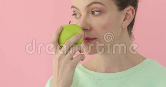 女人在浅粉色背景下嗅着苹果视频的预览图