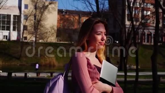快乐的学生带着笔记本电脑和背包慢动作在公园里散步视频的预览图