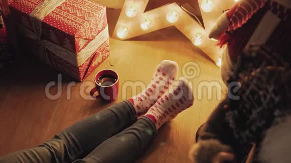 穿着圣诞袜子的女人带着红茶或咖啡在家放松视频的预览图