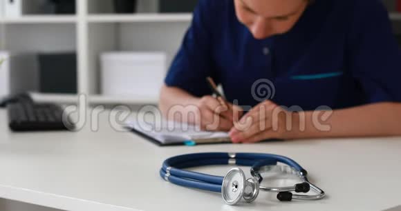 女医生在桌子上填写文件蓝色听诊器在前景视频的预览图