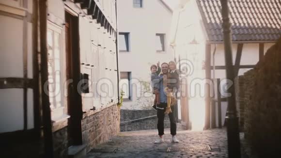 年轻的父亲怀里抱着两个快乐的孩子英俊的欧洲男人男孩和女孩挥手微笑4K视频的预览图