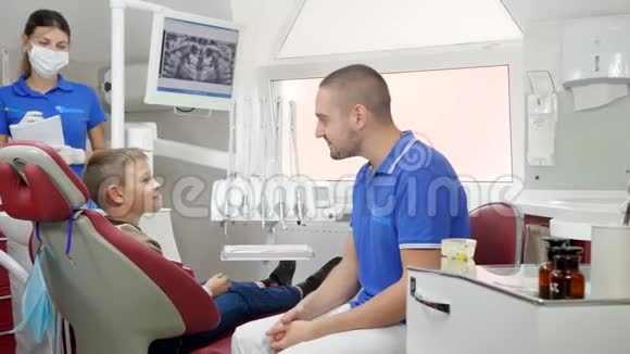 小男孩坐在牙科椅上和好医生和护士交谈手里拿着笔记本视频的预览图