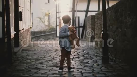可爱的白人男孩在外面唱歌的肖像男孩子看着古老铺成的镇街上的摄像机太阳耀斑4K视频的预览图