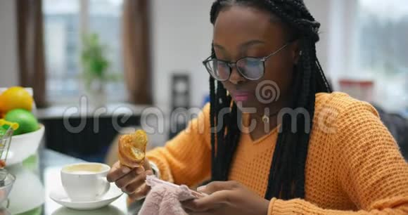 美丽的非洲女孩喝咖啡和羊角面包和聊天电话视频的预览图