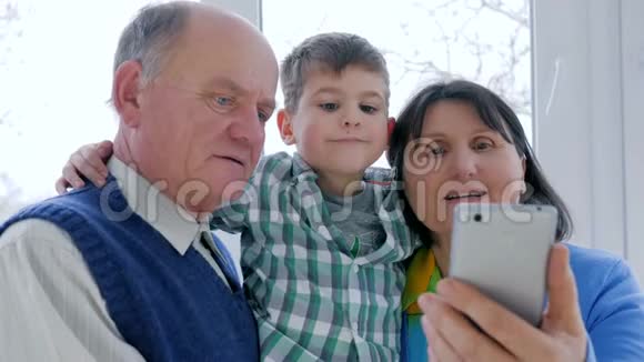 在房间的智能手机里带着可爱的孩子在Skype上聊天微笑着爷爷奶奶视频的预览图
