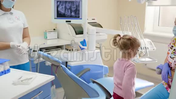 小女孩来到口腔医生坐在仪器和设备旁边的牙科扶手椅上视频的预览图