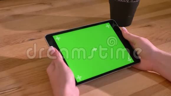 水平平板的特写镜头并在木制桌子背景上的绿色屏幕上手动滑动视频的预览图