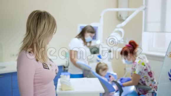 微笑女性在牙科扶手椅中儿童背景和临床医生背景下的肖像视频的预览图