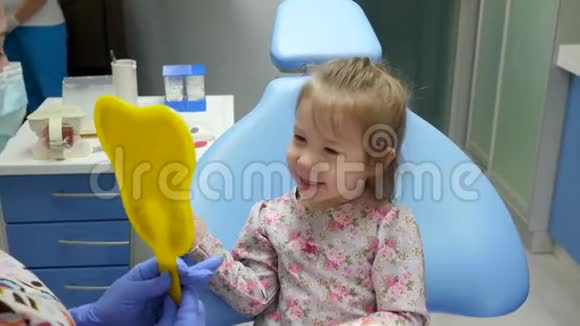 微笑的孩子照镜子坐在牙科椅子上旁边是戴着医疗面具的医生视频的预览图