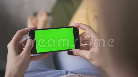 商务亚洲女性手持一部在线绿色屏幕手机躺在家里的沙发上视频的预览图